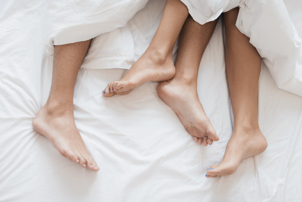 Men and women's legs under a white blanket on a white bed