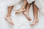 Men and women's legs under a white blanket on a white bed